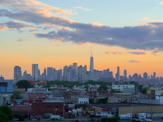 Downtown Manhattan skyline behind an industrial area at dusk, partially cloudy