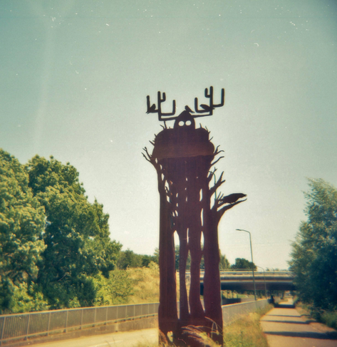 A police of roadside art, made of flat, corrugated, rust colored iron. At first it looks like a weird Viking in a furry cloak standing in the bushes, with a helmet with antlers. On second look, it could also be a group of slender trees with a large bird nest. Small birds (part of the artwork, not real ones) are perched on the antlers. I pad this a few times a year visiting a friend. To me it alwas looks like a slightly bewildered viking that's been lost in the forest for too long.
