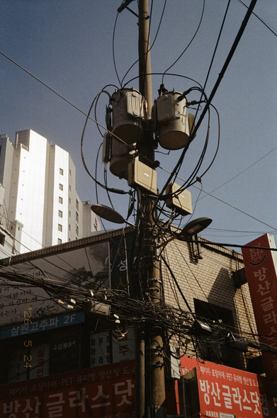 전봇대에 변압기, 조명, 전선들 따위가 복잡하게 뒤엉켜있다. 아래쪽에는 낮은 상가 건물, 뒤쪽에는 고층건물이 보인다. 촬영 날짜는 2026년 5월 24일로 찍혀있다.