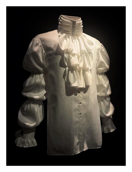 Regency-style white shirt worn by Prince during his 1984 Purple Rain tour, with long puffy sleeves, jabot (a fall of ruffles from the neck), and pearl buttons. The fabric appears to be dotted with tiny holes.

Displayed at the 2025 exhibition “Superfine: Tailoring Black Style” at the Metropolitan Museum of Art in NYC. Details from the museum placard:

Marie France (French, b. 1945)
Louis & Vaughn (American, founded 1981)
Louis Wells (American, 1957-2018)
Vaughn Terry Jelks (American, b. 1950)
Shirt worn by Prince, ca. 1984
White dotted polyester jacquard