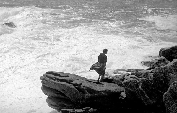 une femme dans le vent, debout sur les rochers surplombant la mer