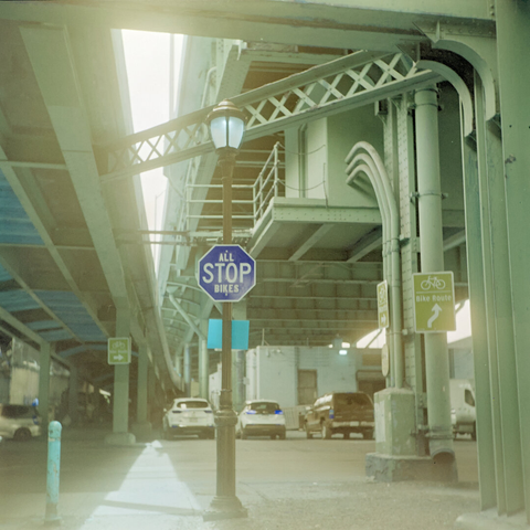 Street beneath great steel bridges that are painted green. This film makes the red stop sign look blue.