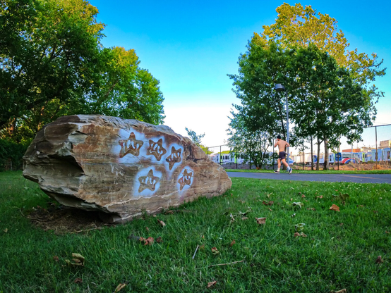 stenciled stars sprayed onto a rock next to a towpath. a man runs shirtless on the path in the background