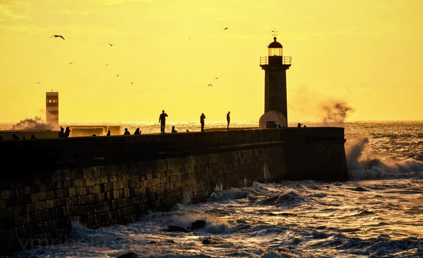 Farolim de Felgueiras na Foz do Douro, com ondas a embater no molhe e o farol iluminado pela luz quente do fim de tarde.