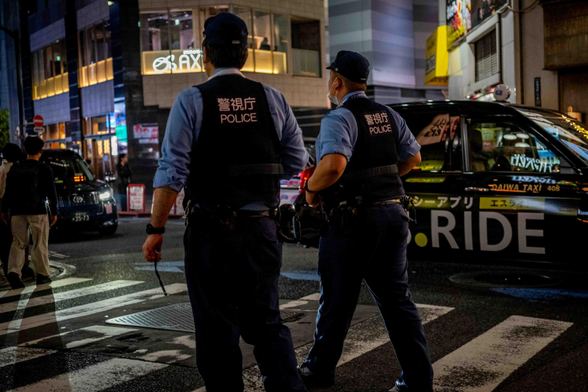 Dos policies caminant enfront d'un taxi amb reflexos als vidres als carrers de Kabukicho.