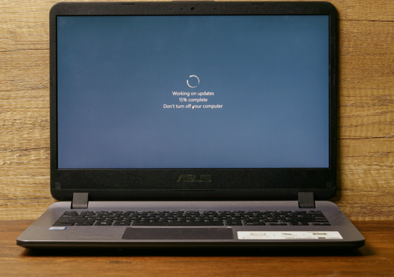 A picture of a Microsoft Windows laptop at the screen "Working on updates, 15 percent complete. Do not turn off your computer." The computer is sitting on top of a wooden desk.