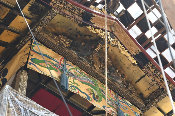鶏鉾の前側の妻板飾り。むかって右に雌を内向きにあらわし尾羽を立てて歩く姿、 むかって左の雄は立って外側を向き、頭を下げて左方に振り何かをついばむ姿。/ 2026.07.14 四条通・月鉾町から