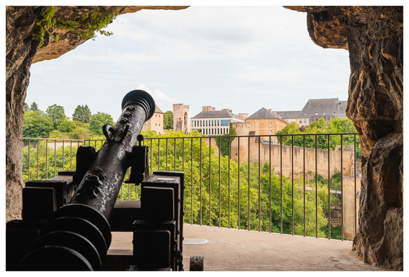 Kanone steht vor einem Loch im Fels und blickt hinab in die Altstadt.