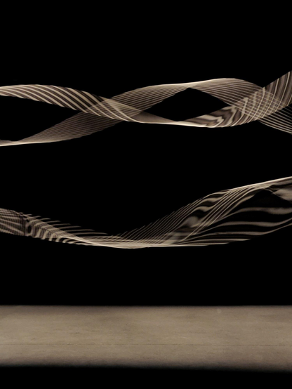 A photo of a dark room with two pairs of  long elastic strings rotating quickly under spotlights. A striped pattern of shadows appears on the motion blurring strings. 