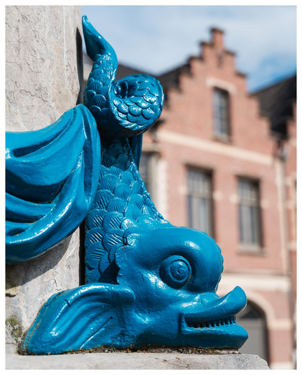 Deko-Element an einem Brunnen: ein blau angepinselter Fisch, vermutlich aus Metallguss.
