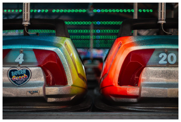 Zwei Boxautos vom Rummel parken nebeneinander. Im Hintergrund sind grüne Lichter zu sehen, die an der Decke hängen.