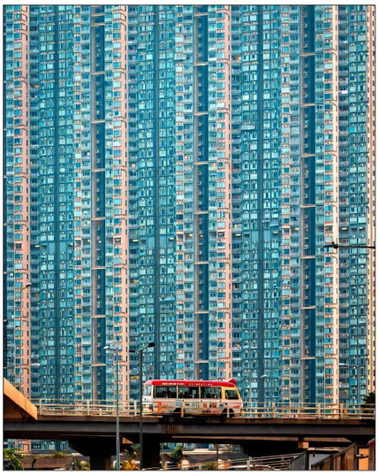 A bus on a bridge, passing by a very tall building.