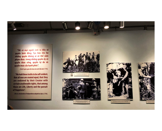 A placard with a sentence from the US Declaration of Independence, in Vietnamese and English — “We hold these truths to be self-evident, that all men are created equal, that they are endowed by their Creator with certain unalienable rights, that among these are Life, Liberty and the pursuit of Happiness” — is mounted on a museum wall, alongside black-and-white photographs of American soldiers rounding up Vietnamese villagers for interrogation.