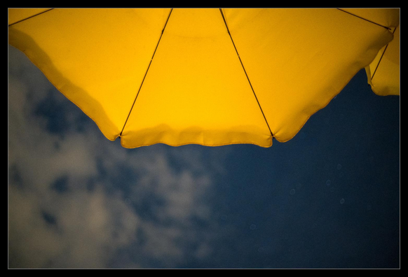 Ein vom Mondlicht beleuchteter gelber Sonnenschirm vor dem blauen Nachthimmel.