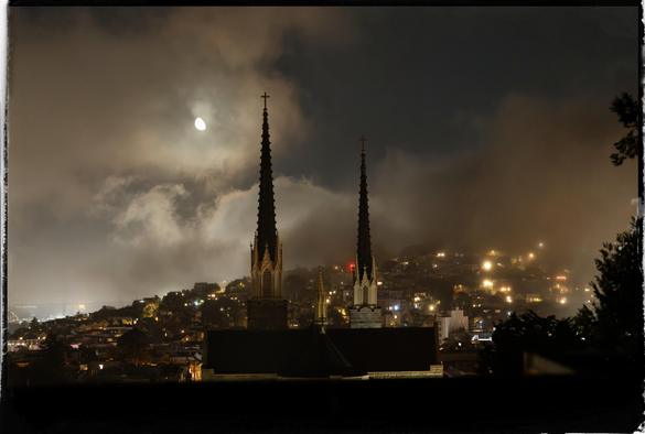A picture of the fog rolling in across a cityscape at night, with the moon and the fraternal twin spires of Saint Paul's Catholic Church in the center of the picture. The fog, locally known as Karl, has obscured the view of Bernal Heights as it creeps across the city. 

Add: Karl, contrary to the poem, does not come in on little cat feet. It wears hiking boots and it moves quite quickly. 15 minutes after this picture was taken, the cityscape was completely hidden behind a wet gray blanket.