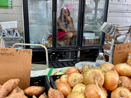 A woman sits inside a produce fridge at a market.