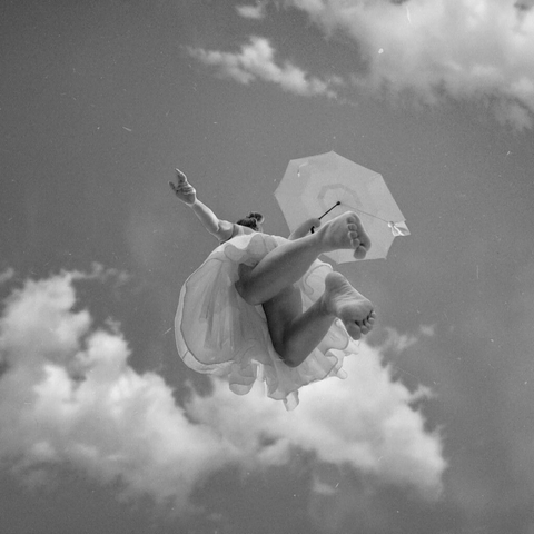 une femme tenant une ombrelle, les bras écartés, plane entre les nuages