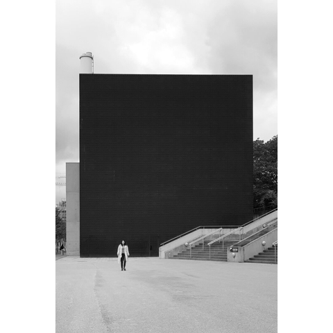 Black and white street photography taken in Luxembourg city showing a woman walking in front of the black concrete building of Luxenergie.
