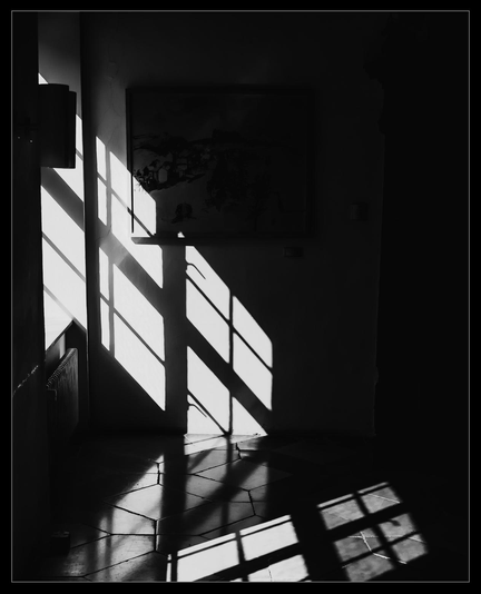 Sehr kontraststarkes s/w Bild. Die Sonne projiziert die Sprossen eines Fensters auf Wand und Fußboden.