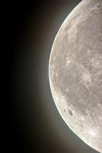 Image of the western section of the moon at right, its curved horizon emitting a soft glow into the darkness at left. Prominent features include the bright spot of Aristarchus Crater in the upper half, the larger, darker spot of Grimaldi Crater in the lower half, and Plato Crater at the upper right corner.

Shot on an iPhone 15 attached to a Celestron 130mm-aperture reflector telescope.
