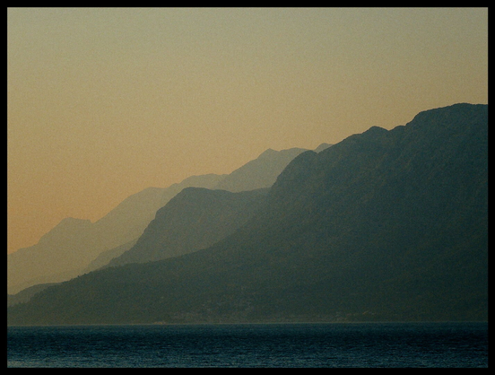 Meer, Berge im Dunst und orangener Abendhimmel