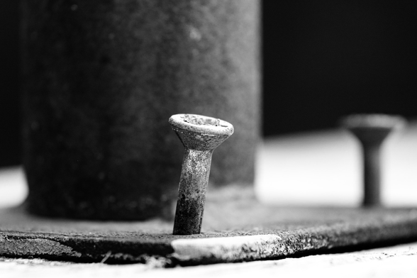 A close-up, black and white image of a weathered screw in a metal surface.