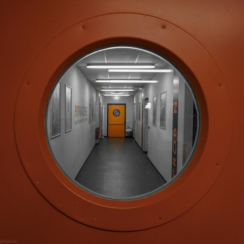 Orange Tür mit rundem Fenster drin auf einem weißen Flur