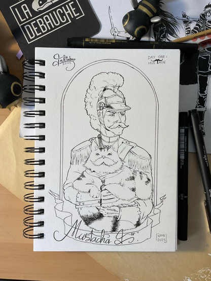 Photo d’un carnet de dessin sur un bureau
Y ont été dessinés un homme moustachu en uniforme de dragon (les cavaliers, pas le monstre) portant un gros chat avec une médaille dans les bras. Le chat a la même moustache que l’homme. Le nom « Mustacha 1er » est inscrit en dessous
