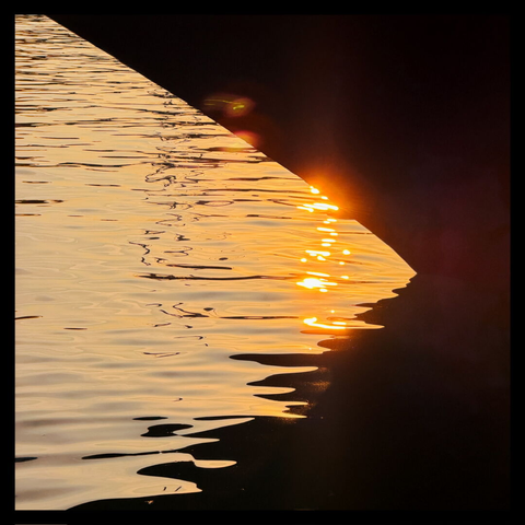 Zwischen Bug und Wasseroberfläche scheinen Reflexionen der untergehenden Sonne durch
