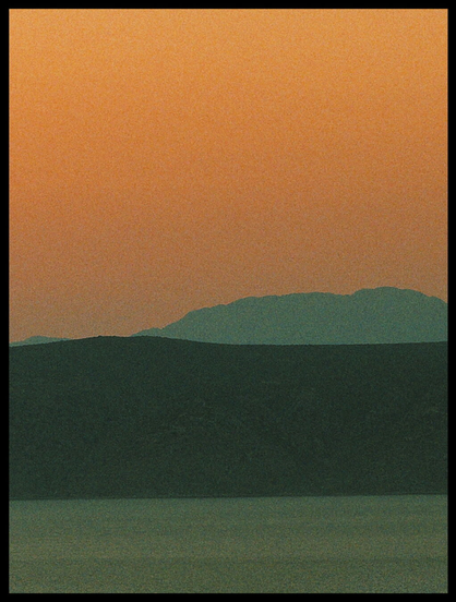 Oranger Abendhimmel mit Bergen im Dunst und davor Meer