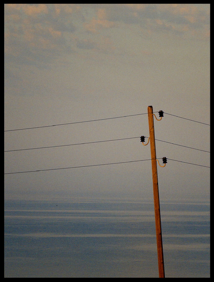 Golden orange angestrahlter Strommast mit Meer und diffusem Himmel dahinter