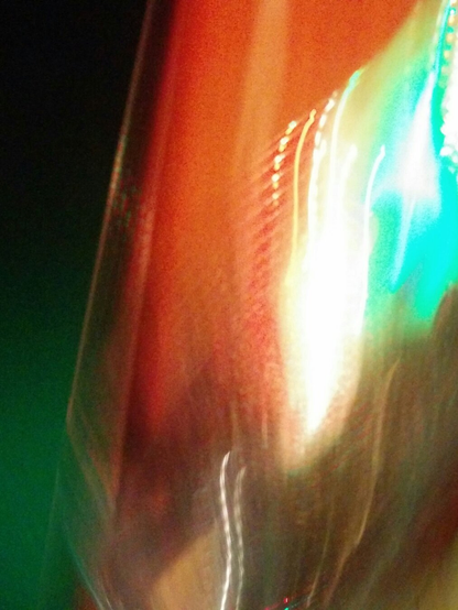 An abstract, blurry photograph showing distorted light leaks and motion blur in vivid colours of emerald green, vibrant red, bright white, and turquoise green.