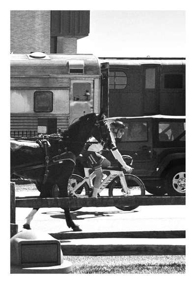 Black and white photo of four modes of transportation. In front is a horse with a harness and blinders, trotting along a street and pulling a wagon that’s out of frame. Right behind and pulling slightly ahead of it is a helmeted cyclist on a bicycle. Beyond the cyclist is a boxy car going in the other direction. Behind the car are two railcars of an old-fashioned steam engine train.

Photo taken at historic Strasburg Rail Road in Lancaster, Pennsylvania.