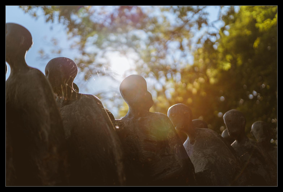 Eine Gruppe menschliche Figuren im Gegenlicht fotografiert. Im Hintergrund Bäume und Himmel.