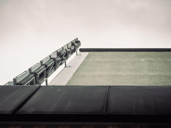 Schwarz-Weiß-Aufnahme einer Gebäudefassade von unten. Eine alte Leuchtreklame zieht sich diagonal in den hellen, nahezu weißen Himmel.