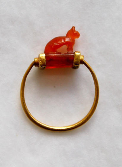 A gold ring with a red translucent gemstone featuring a small cat-shaped figure on top.
