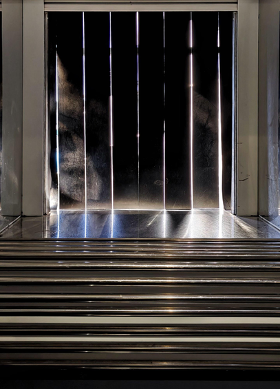 A photo of a pass-through door with black rubber strips hanging vertically down. Bright sunlight is seeping through the gaps in between and below the strips.