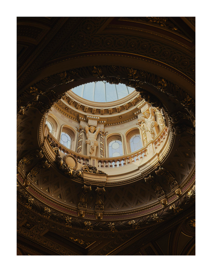 Looking up at a glass dome in a golden coloured, ornate ceiling.