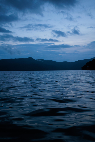 Calm lake water with gentle ripples under a cloudy twilight sky, silhouetted mountains in the distance.