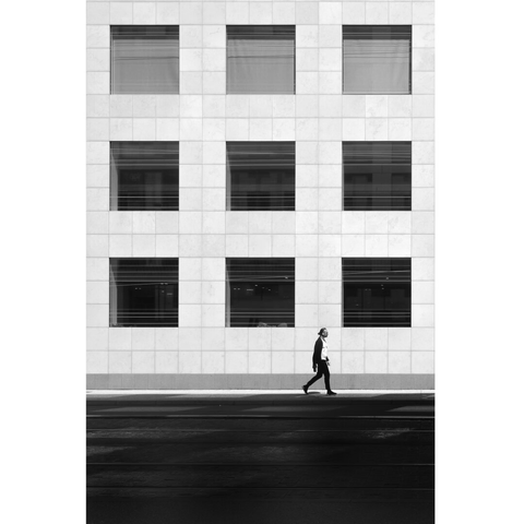 Black and white street photography taken in Luxembourg city showing a man walking on the pavement under a perfect minimal square formed by 9 square windows.