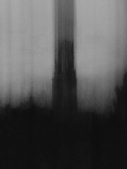 A black and white picture of a semi-abstract scene. A dark tower and trees, smeared by moving the camera while taking a low shutter speed picture.