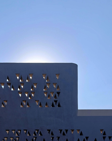 A photo of the sun behind (being eclipsed) a modern architectural structure featuring a geometric pattern of triangular cutouts. The sky in the background is a clear pale blue.