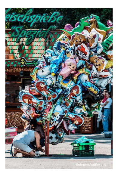 Man sieht Strauß von sicher 100 Ballons. Lustige Gestalten und Tiere. Zwei Personen Knoten sie fest, damit sie nicht wegfliegen.