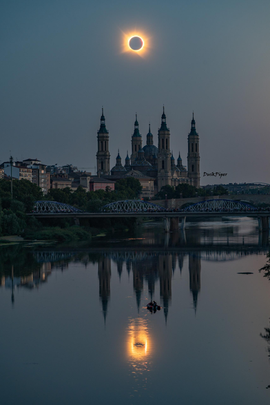 2026 August 13
The Moon covers the Sun in the middle of the sky above an ornate church. A ring of bright whisps from the Sun's corona surrounds the Moon. In front of the church is a river that shows ripples across the eclipse's reflection. Some people are boating in the river.

Total Solar Eclipse Over Spain
 * Image Credit & Copyright: Ruiyu Zhang
 * Text: Keighley Rockcliffe (NASA GSFC, UMBC CSST, CRESST II)

Explanation: 
On August 12th, 2026, the Moon totally eclipsed the Sun and cast its shadow across Siberia, Greenland, Iceland, Spain, and Portugal. Today’s image features two total solar eclipses viewed from Zaragoza, Spain, one over the Cathedral-Basilica of Our Lady of the Pillar and the other reflecting in the Ebro River. For a few moments, Spain saw its first major total solar eclipse since 1905. Those witnessing totality may experience a chill in the air, the quieting of birds, the confused chirps of insects, and the shared awe of many. It’s the corona’s time to shine as the Sun’s bright disk is blocked by the Moon. Among other reasons to study eclipses, they help scientists understand why the corona is millions of degrees hotter than the Sun’s surface. Enthusiastic citizens can contribute to these studies by recording how wildlife responds, imaging the corona, and monitoring air temperature and clouds. 

Authors & editors: Robert Nemiroff (MTU) & Jerry Bonnell (UMCP)
NASA Official: Amber Straughn Specific rights apply.
NASA Web Privacy, Accessibility, Notices;
A service of: ASD at NASA / GSFC,
NASA Science Activation
& Michigan Tech. U.