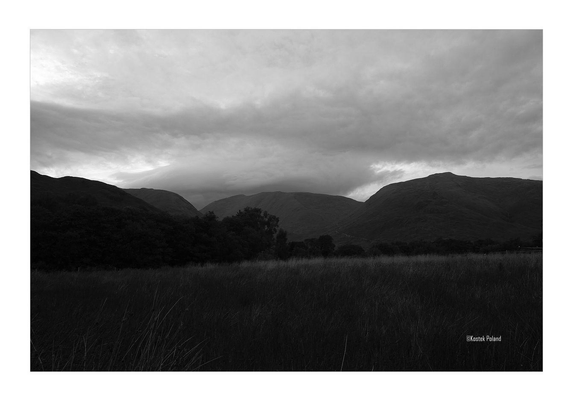 Dalmally, Scotland. Image of an open space with hills, clouds, and some trees.
