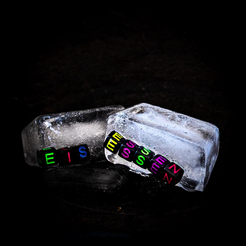 Zwei teilweise geschmolzene Eisblöcke, die jeweils bunte Buchstabenperlen enthalten. Die Perlen buchstabieren die deutschen Worte "EIS" und "ESSEN" vor einem dunklen Hintergrund, was einen auffälligen Kontrast erzeugt.

Two partially melted ice blocks, each containing colourful letter beads. The pearls spell the German words "ICE" and "ESSEN" against a dark background, which creates a striking contrast.