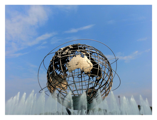 The giant globe of the Unisphere stands under a blue sky with white clouds, above a line of fountains spouting vertical jets of water. The sculpture consists of stainless steel land masses affixed to curved metal beams representing longitude and latitude lines, and is encircled by three rings representing the orbits of Yuri Gagarin and John Glenn (the first Russian and American in space) and the first communications satellite. Our view is such that Australia and Antarctica are most visible, with the other land masses appearing in reverse on the other side of the globe’s mesh of beams.