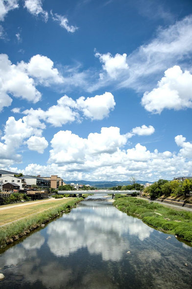 三条大橋から北を向いた景色。奥に写っている橋は御池大橋。鴨川には青空と雲が浮かんだ様子が映り込んでいる。/ 2026.08.14 三条大橋から