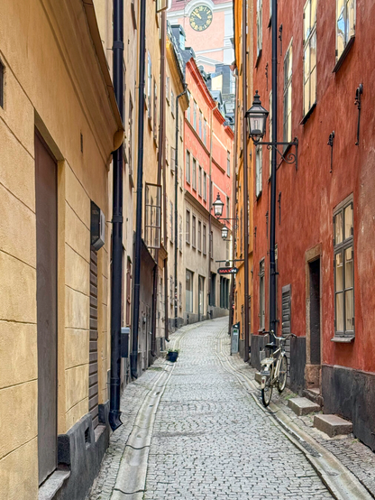 A narrow alley with stone pavers runs through historic buildings with façades in yellow and red. A single bicycle leans against a wall.