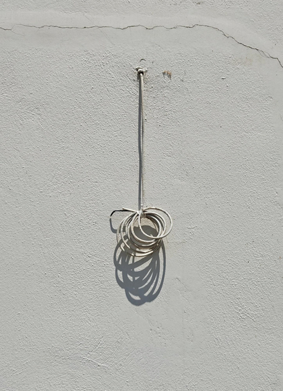A white cable coming out of a white wall, hanging down and the end being coiled up. 